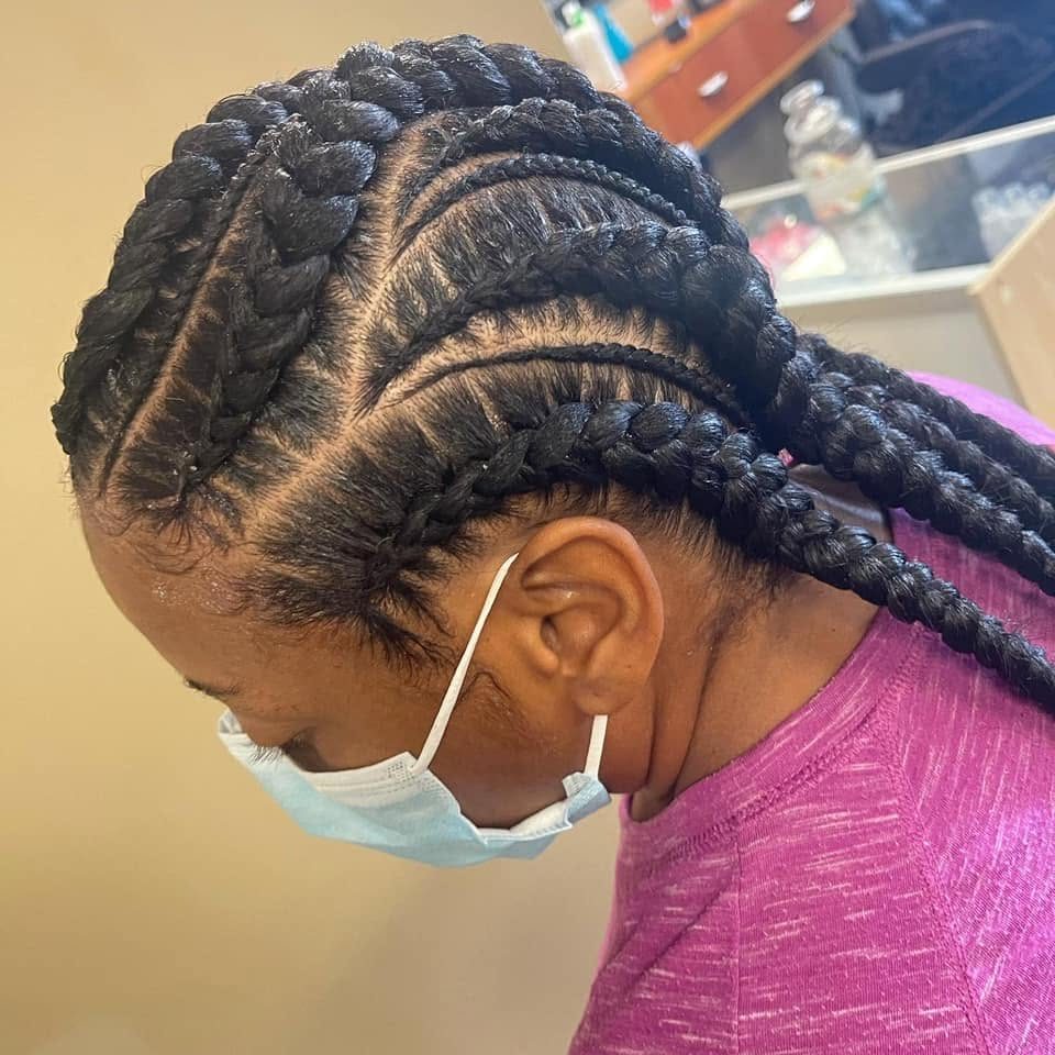 Woman wearing purple shirt with braided hairstyle and face mask, side profile view