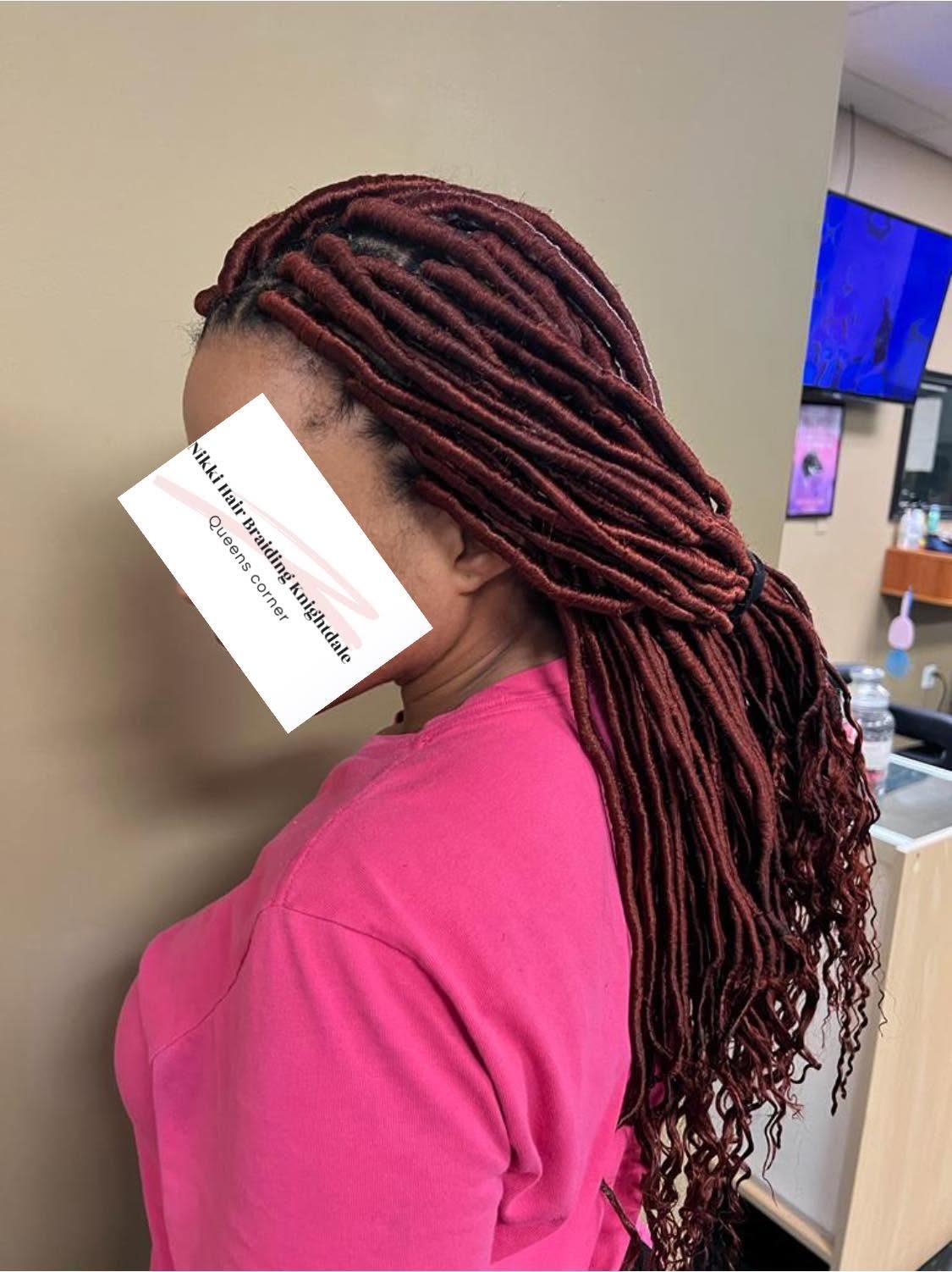 Person with burgundy dreadlocks wearing pink shirt, holding business card in interior space