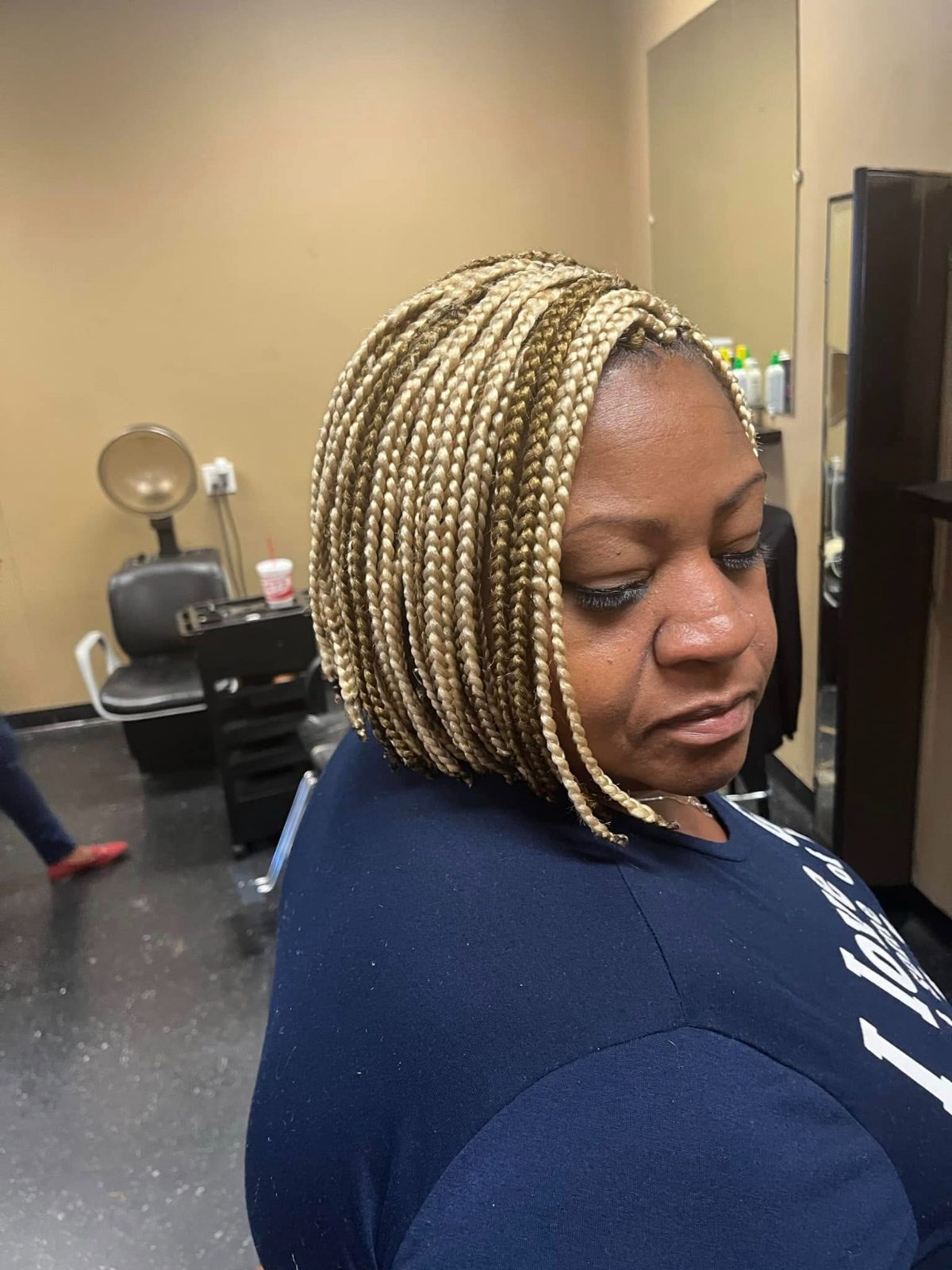 Woman with blonde box braids in a salon, wearing dark blue shirt