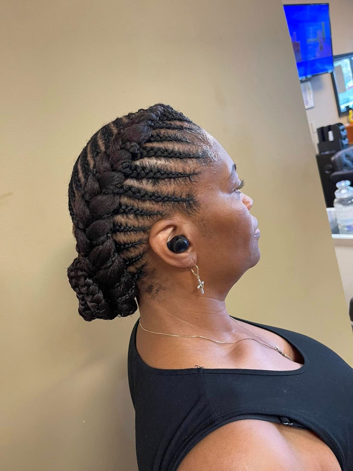 Woman with cornrow braids styled in a braided bun, shown in profile view wearing black top