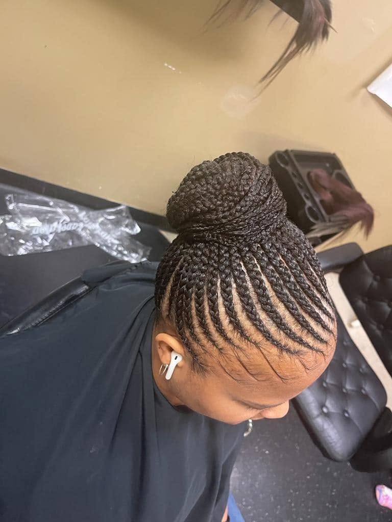 Woman wearing white earbuds with cornrow braids styled in an updo bun