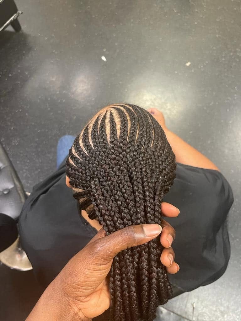 Back view of cornrow braids styled in a ponytail held by a hand