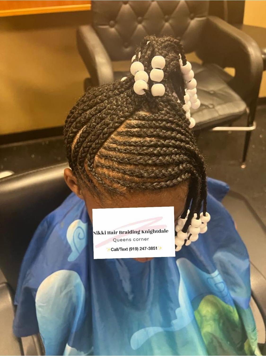Child with braided hairstyle featuring white beads at the ends, wearing blue shirt