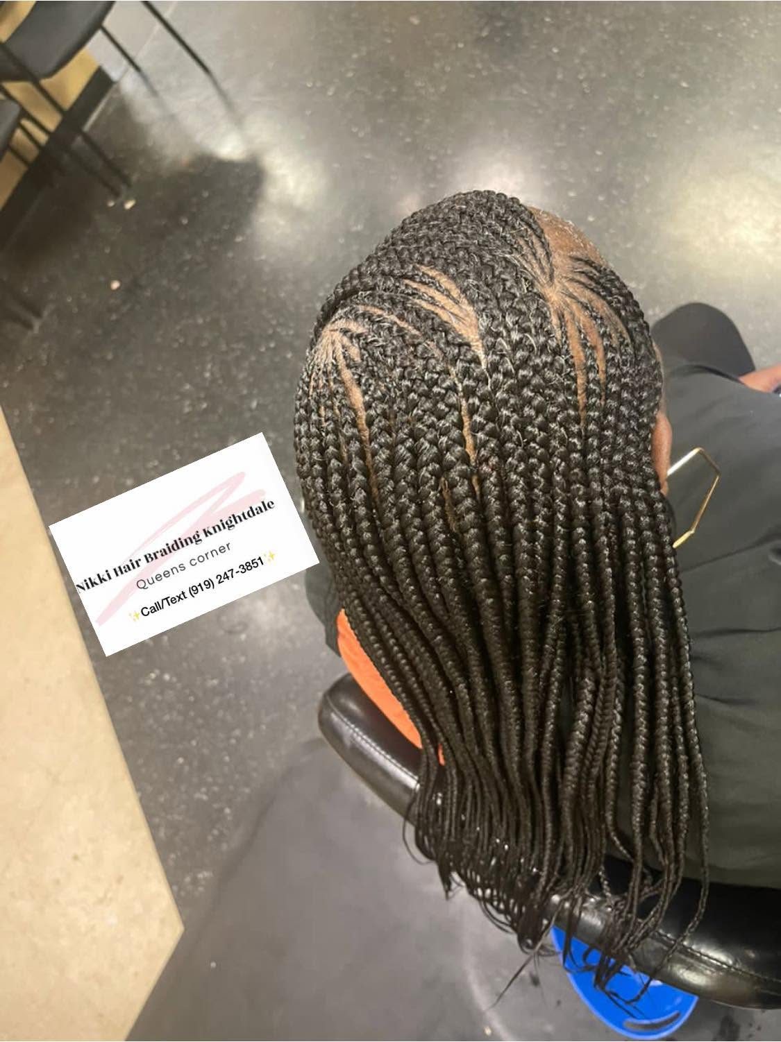 Back view of long braided hairstyle with gold accents and business card for Nikki Hair Braiding displayed
