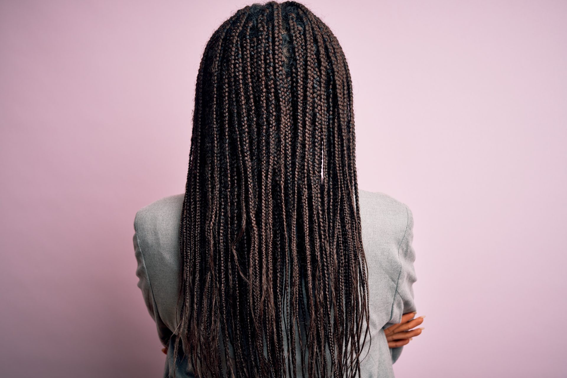 Woman with long box braids wearing gray blazer against pink background