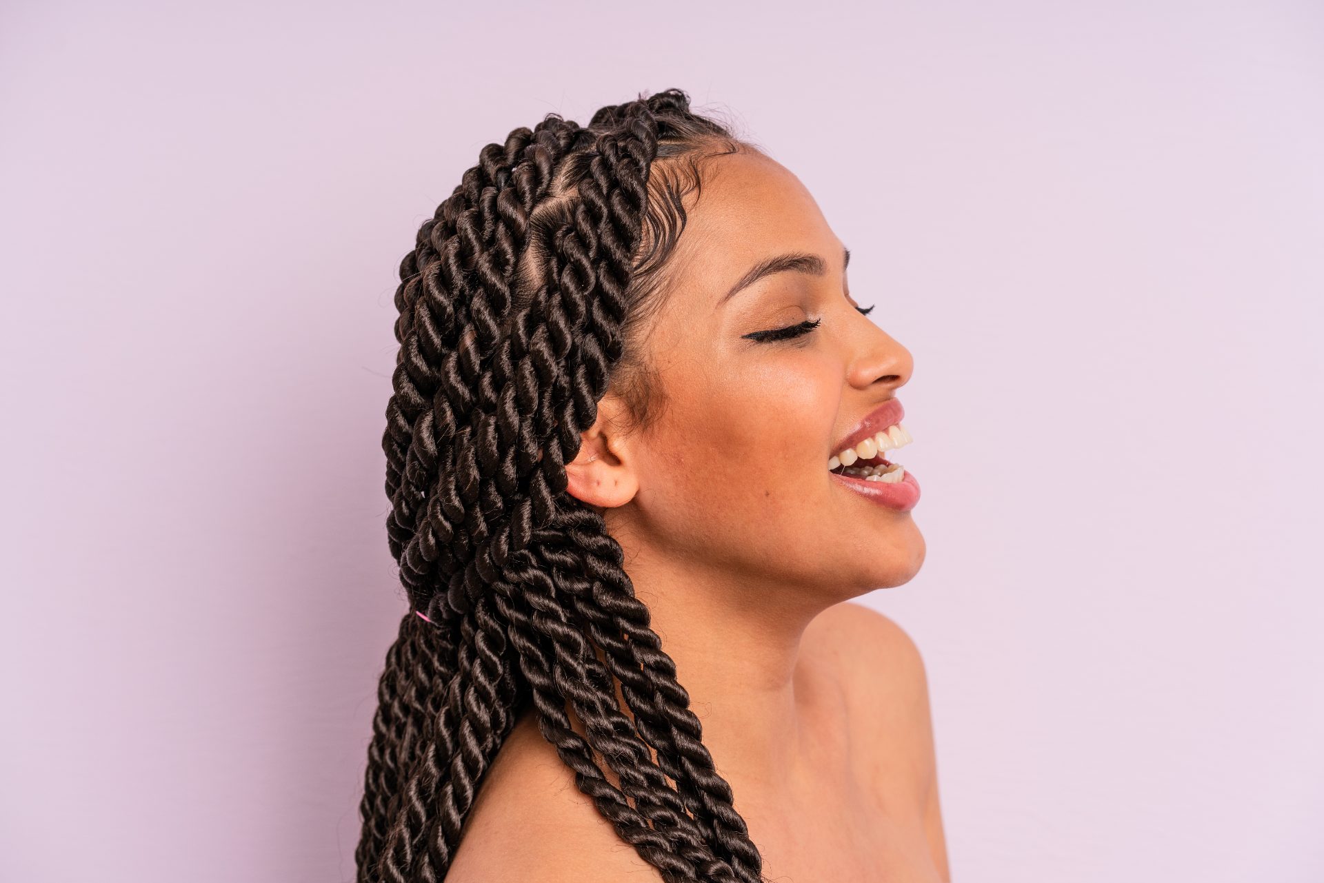 Woman with twisted braids hairstyle smiling in profile against purple background