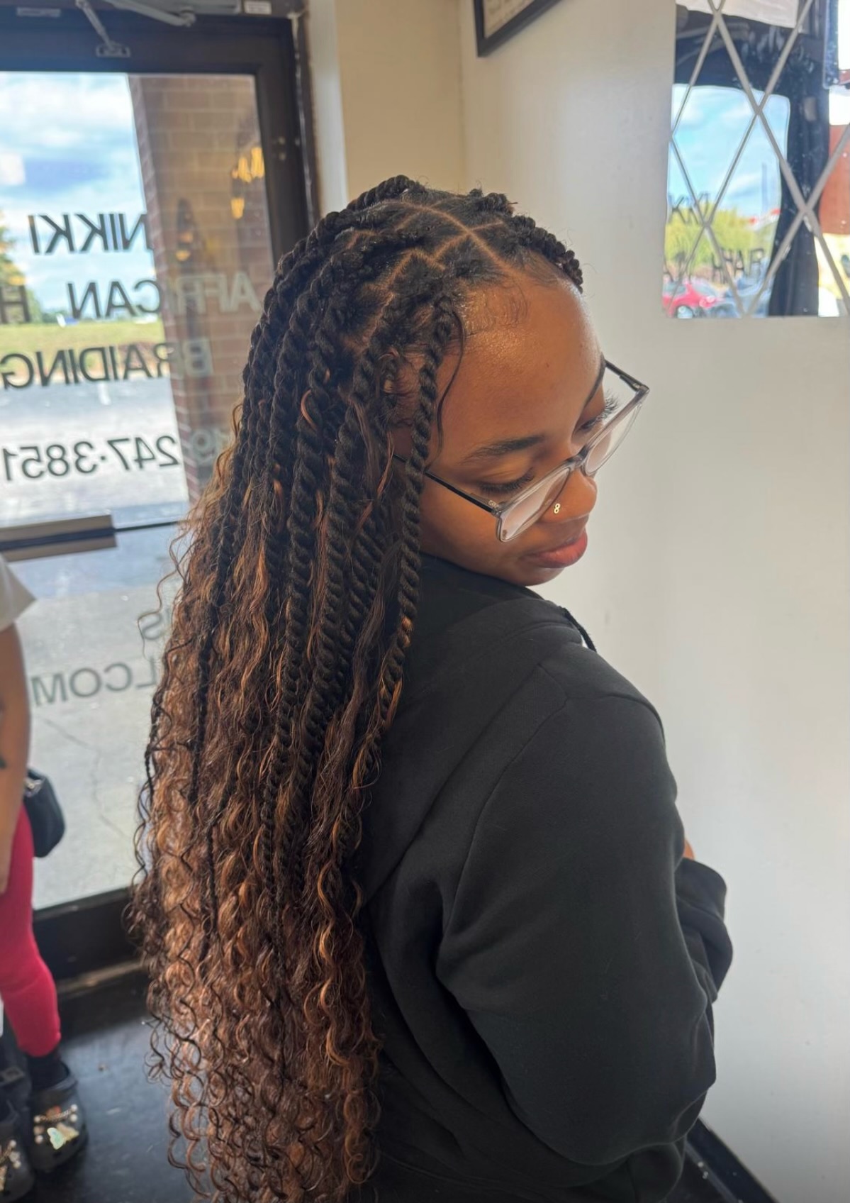 Woman with long braided hair extensions wearing glasses in a salon interior