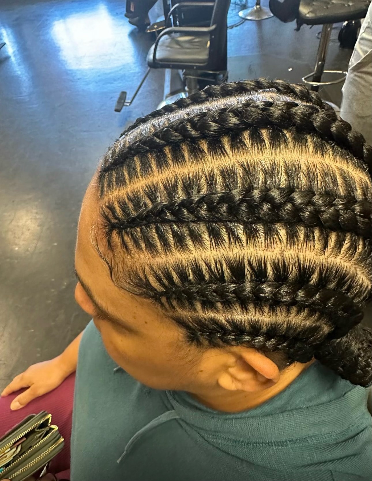Person with braided hairstyle featuring multiple horizontal cornrows in a salon setting