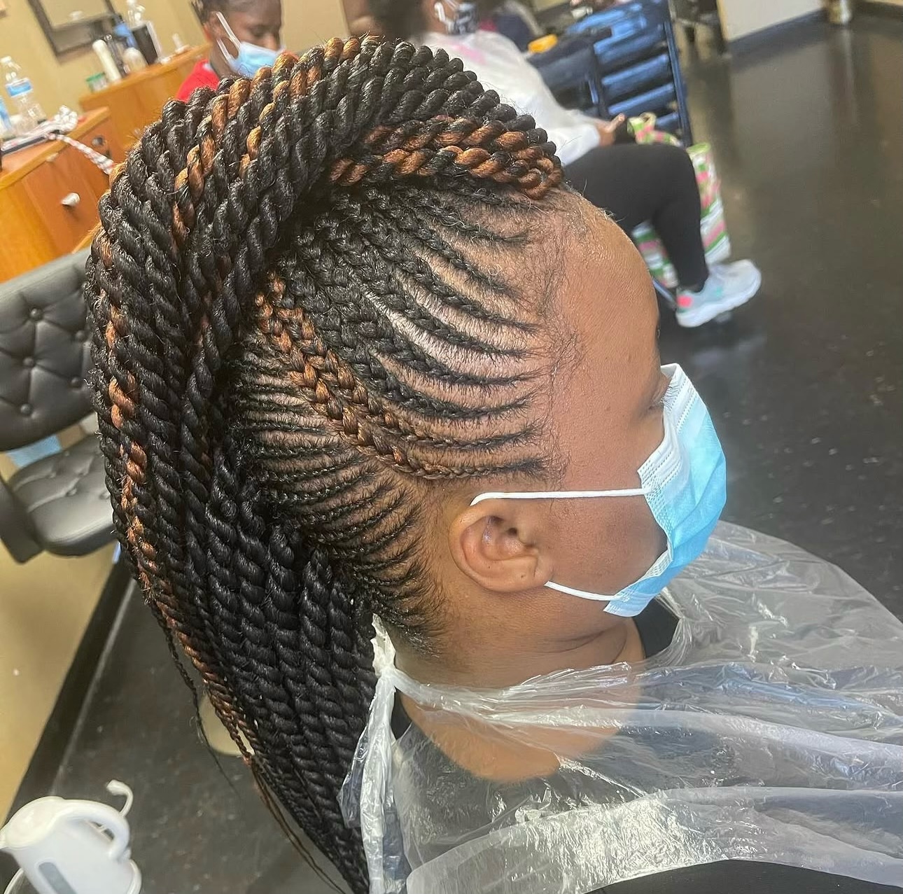 Woman wearing blue face mask displaying twisted braided hairstyle in salon setting