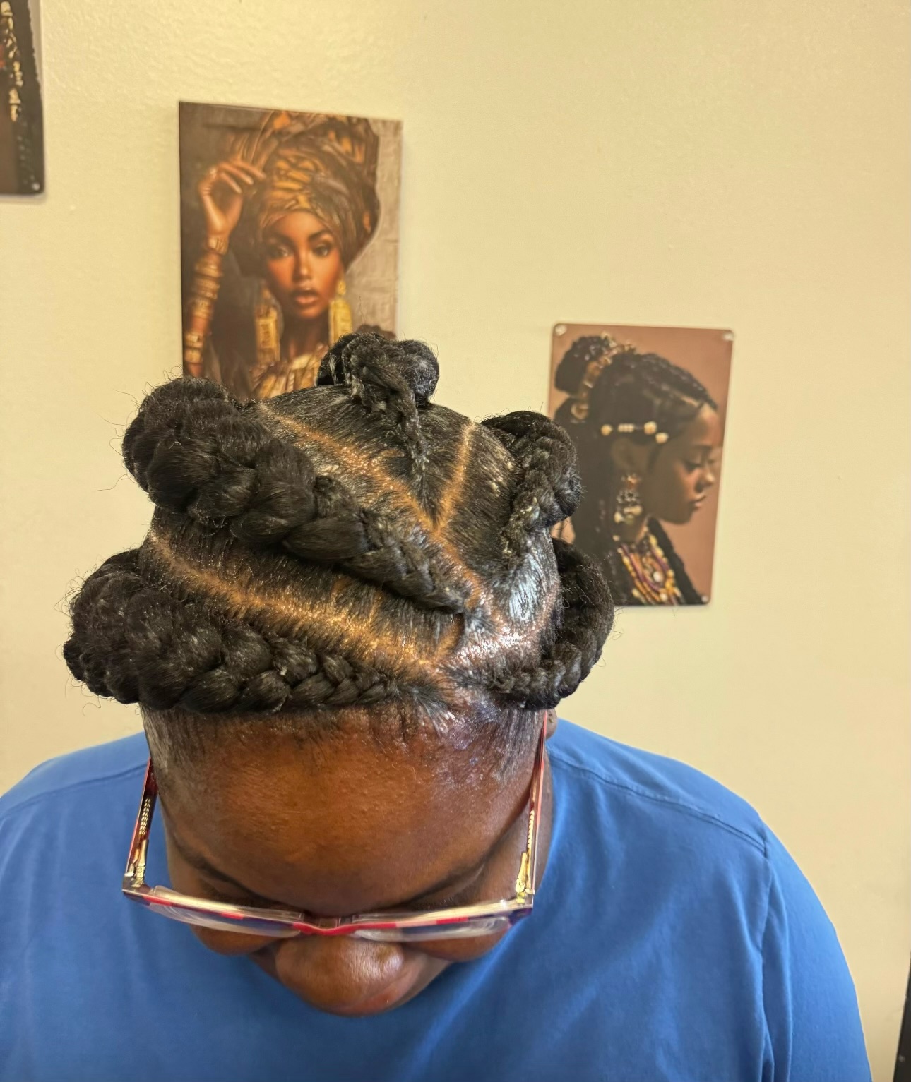 Woman wearing blue shirt with braided updo hairstyle and sunglasses on head, facing away from camera