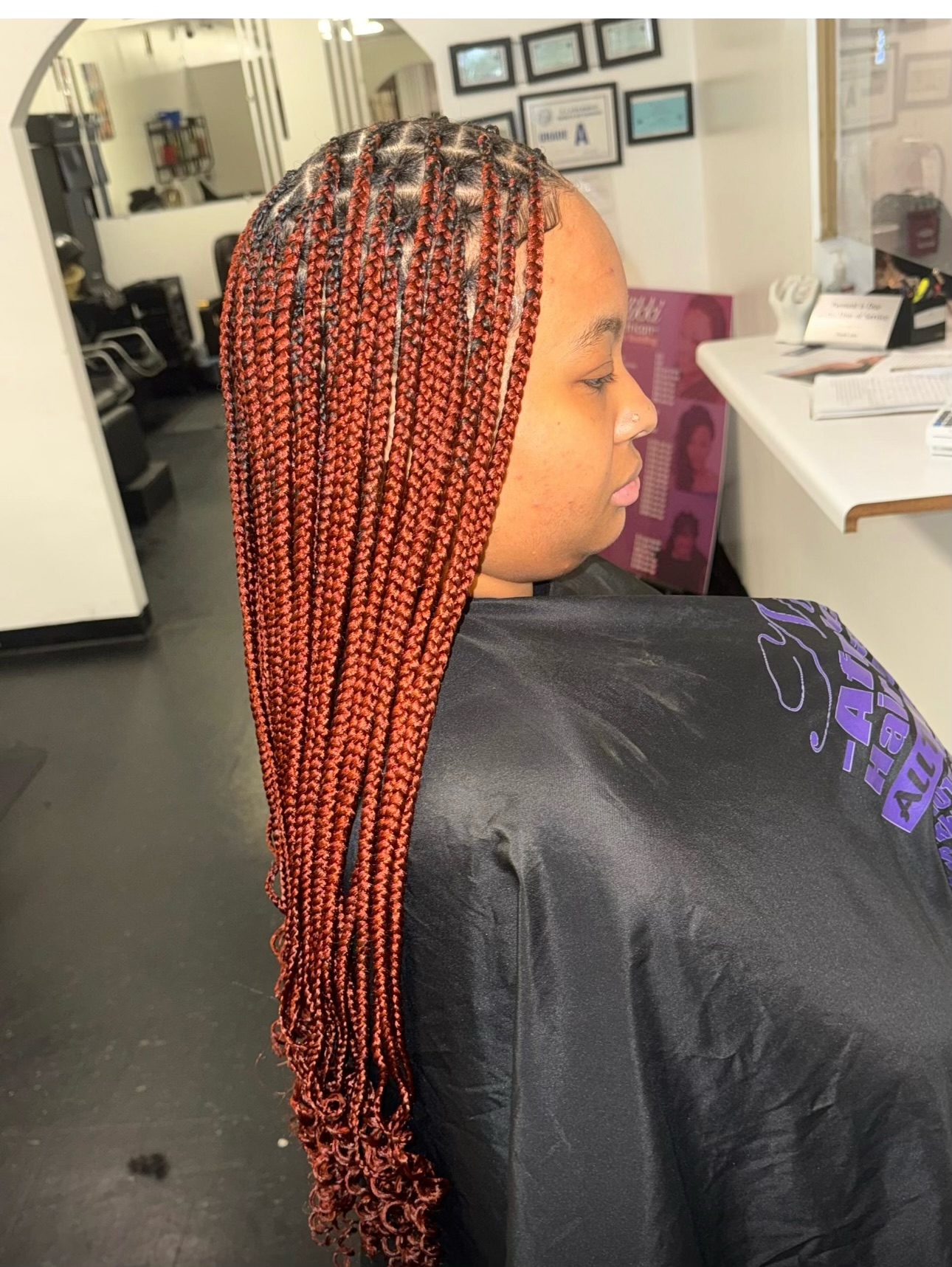 Woman with long red box braids in an office setting, shown in profile view