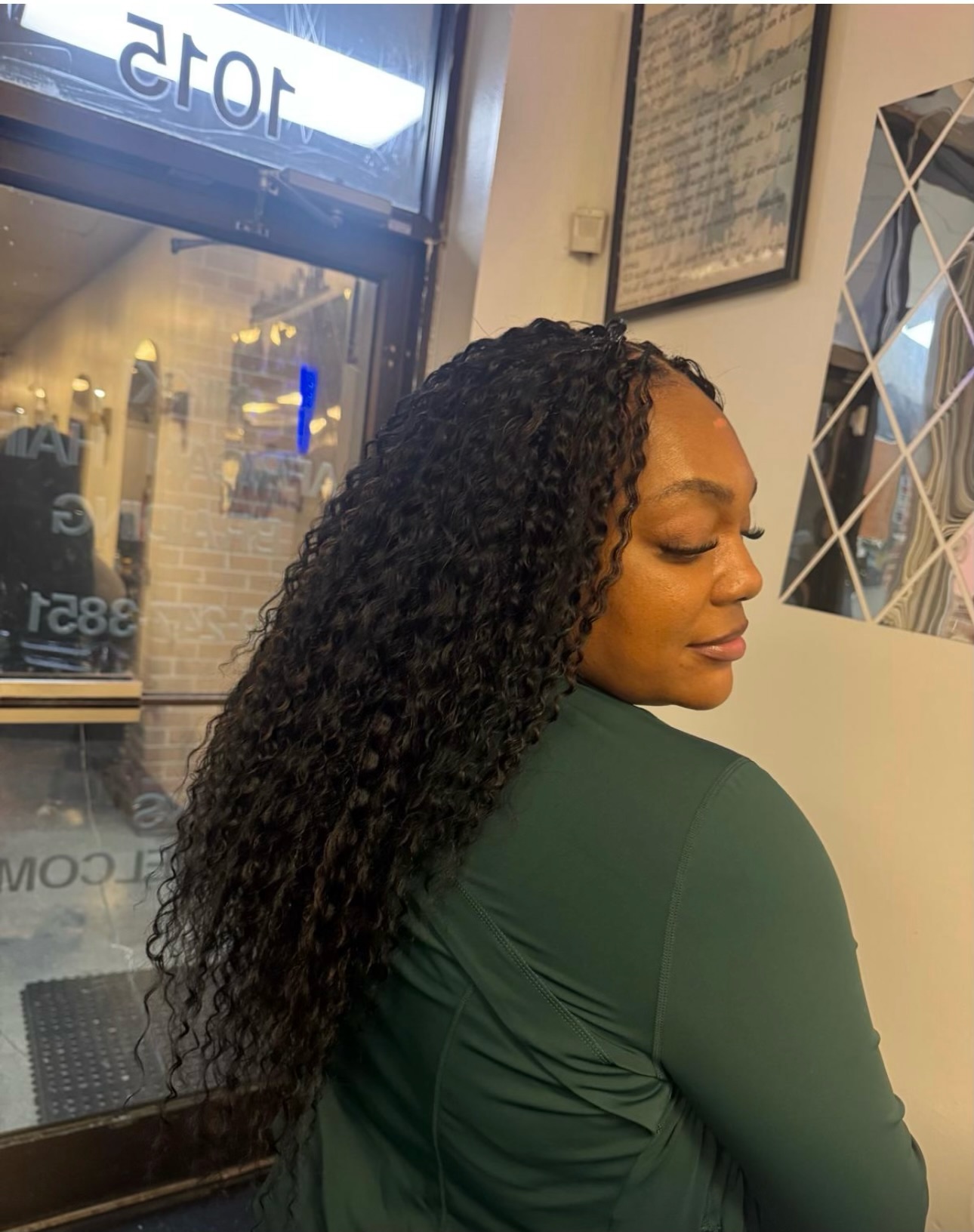 Woman with long curly black hair wearing green shirt, standing in front of storefront