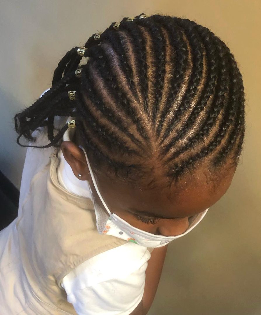 Child wearing white shirt with braided hairstyle adorned with gold beads, photographed from side angle