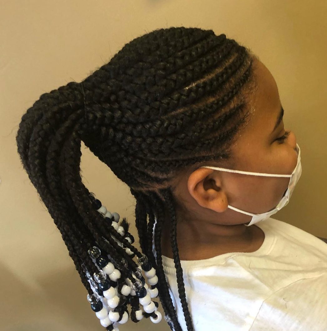 Child wearing white mask with braided hairstyle adorned with white beads