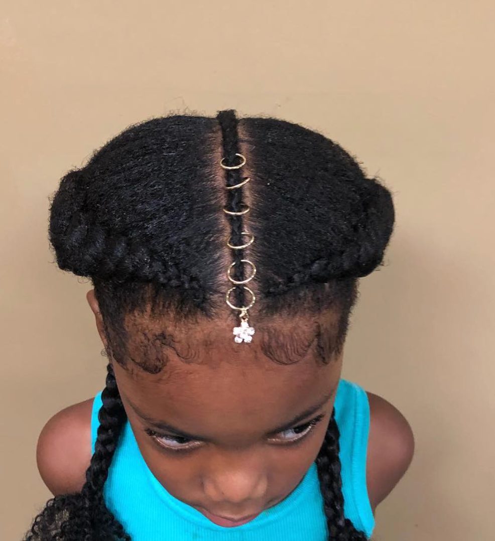 Child's updo hairstyle with cornrows, gold hair rings, and white flower charm pendant