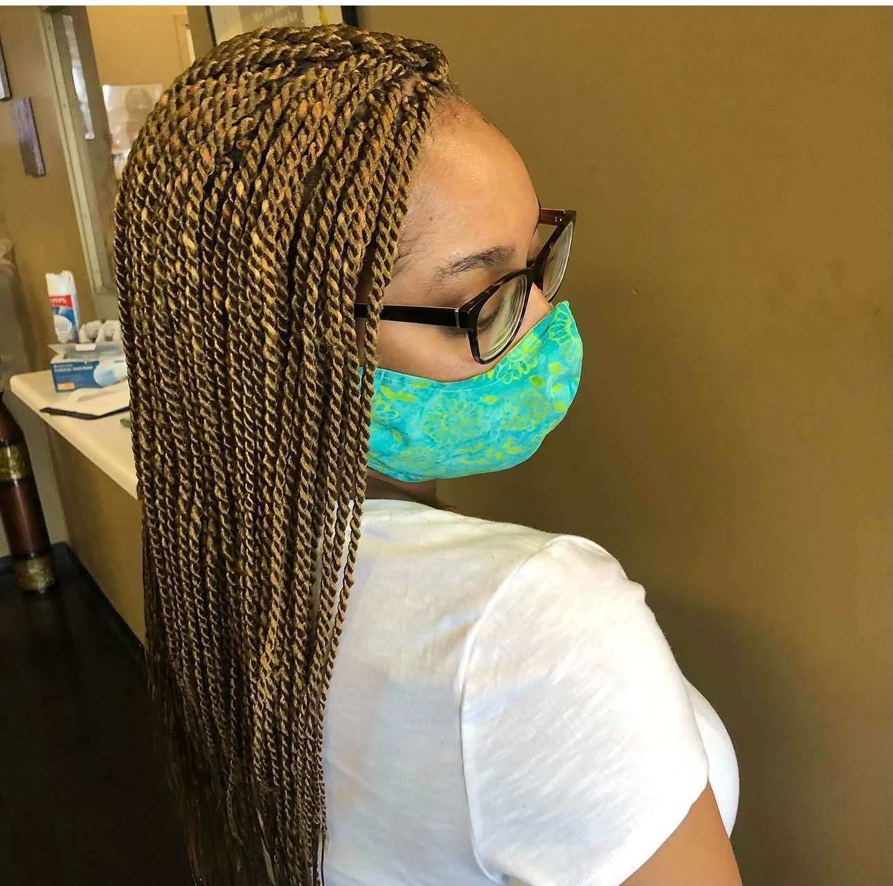 Woman wearing glasses and turquoise mask with long braided hair in medical office