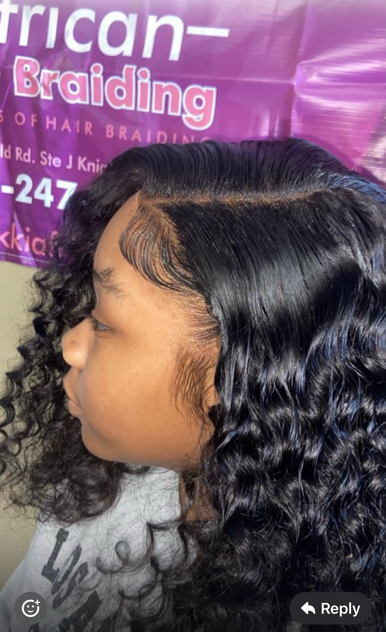 Side profile of woman with long black wavy hair and defined hairline at African braiding salon